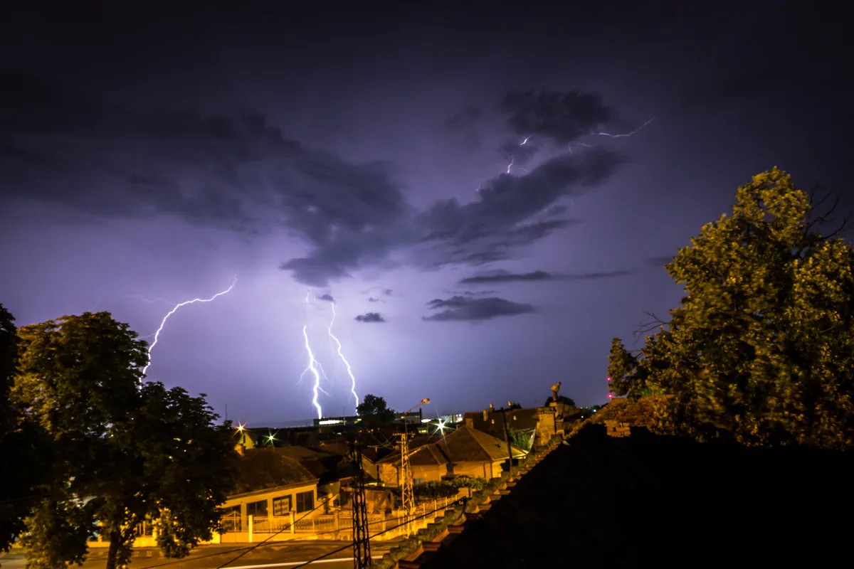 Lightning bolts striking during a night thunderstorm over trees and homes